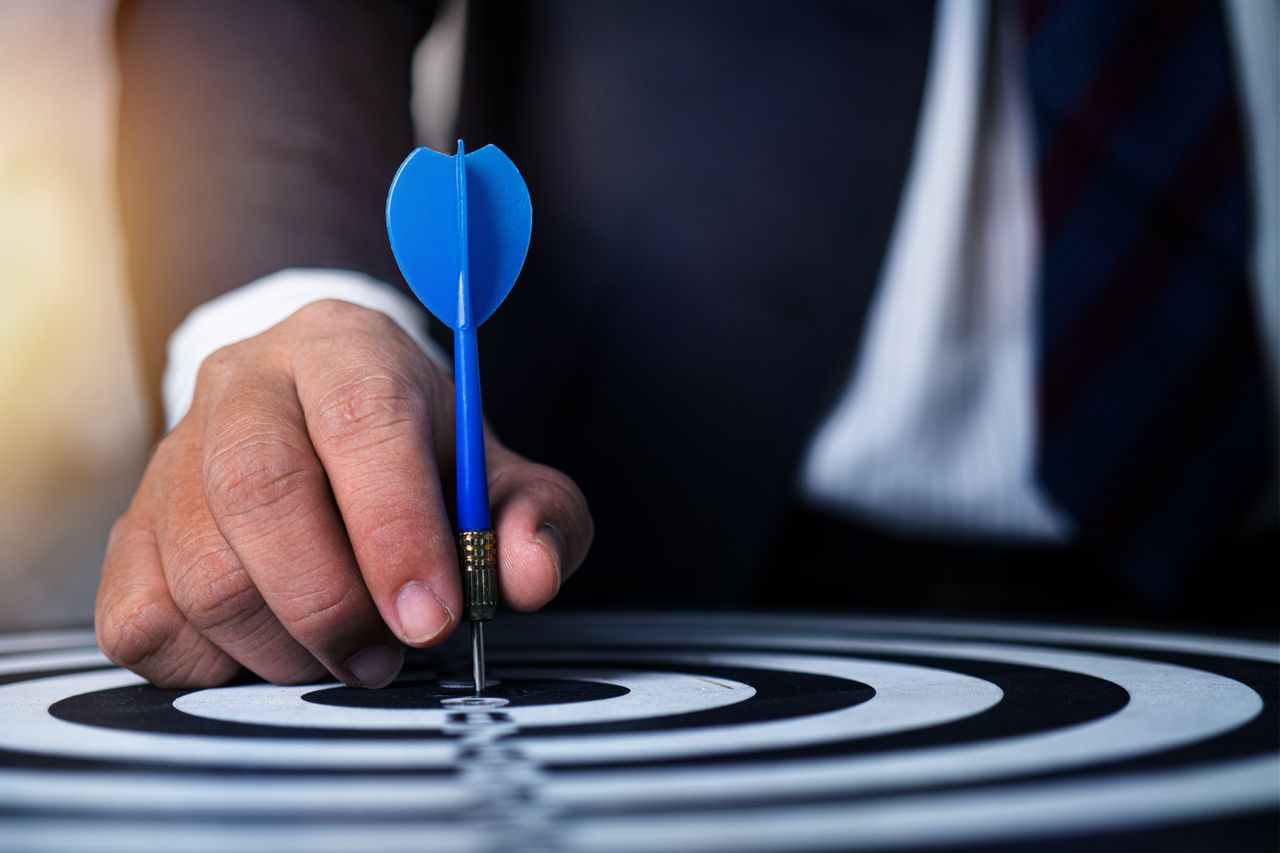 Mastering the First Impression: Your intriguing post title goes here Close-up of a man's hand holding a blue dart on a bullseye, symbolizing precision and focus.