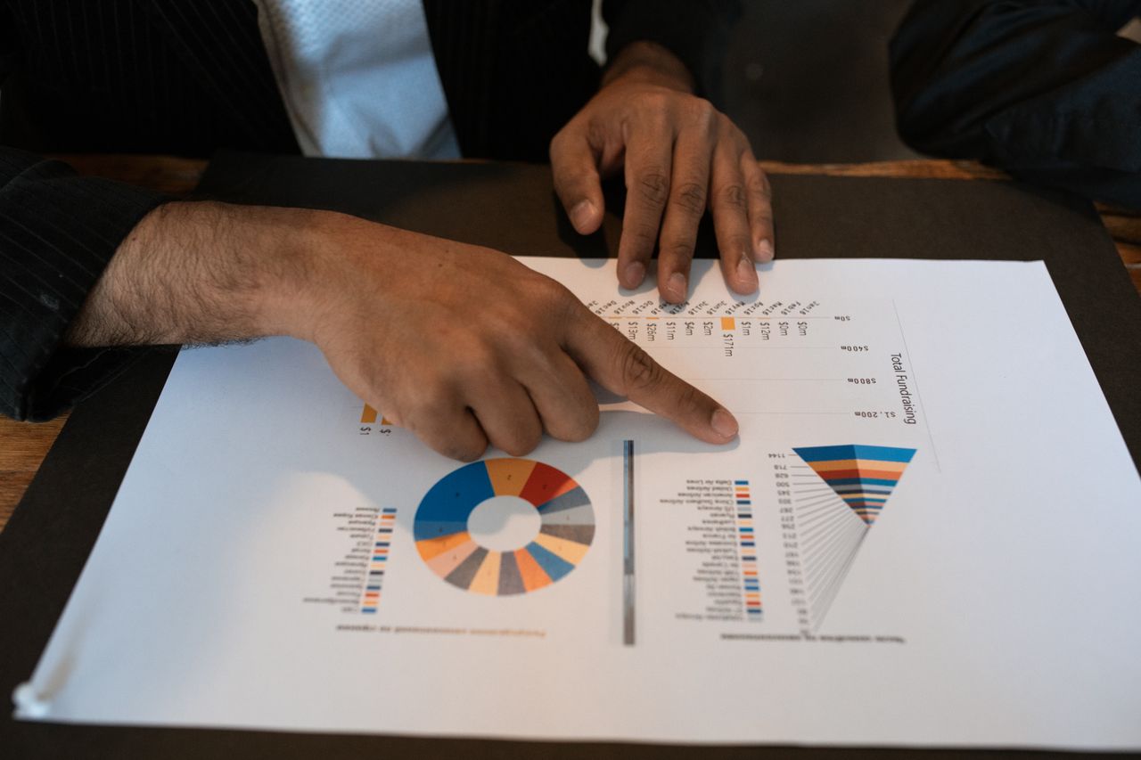 Menus Hands pointing at colorful graphs and charts in a workspace. Ideal for business presentations and reports.